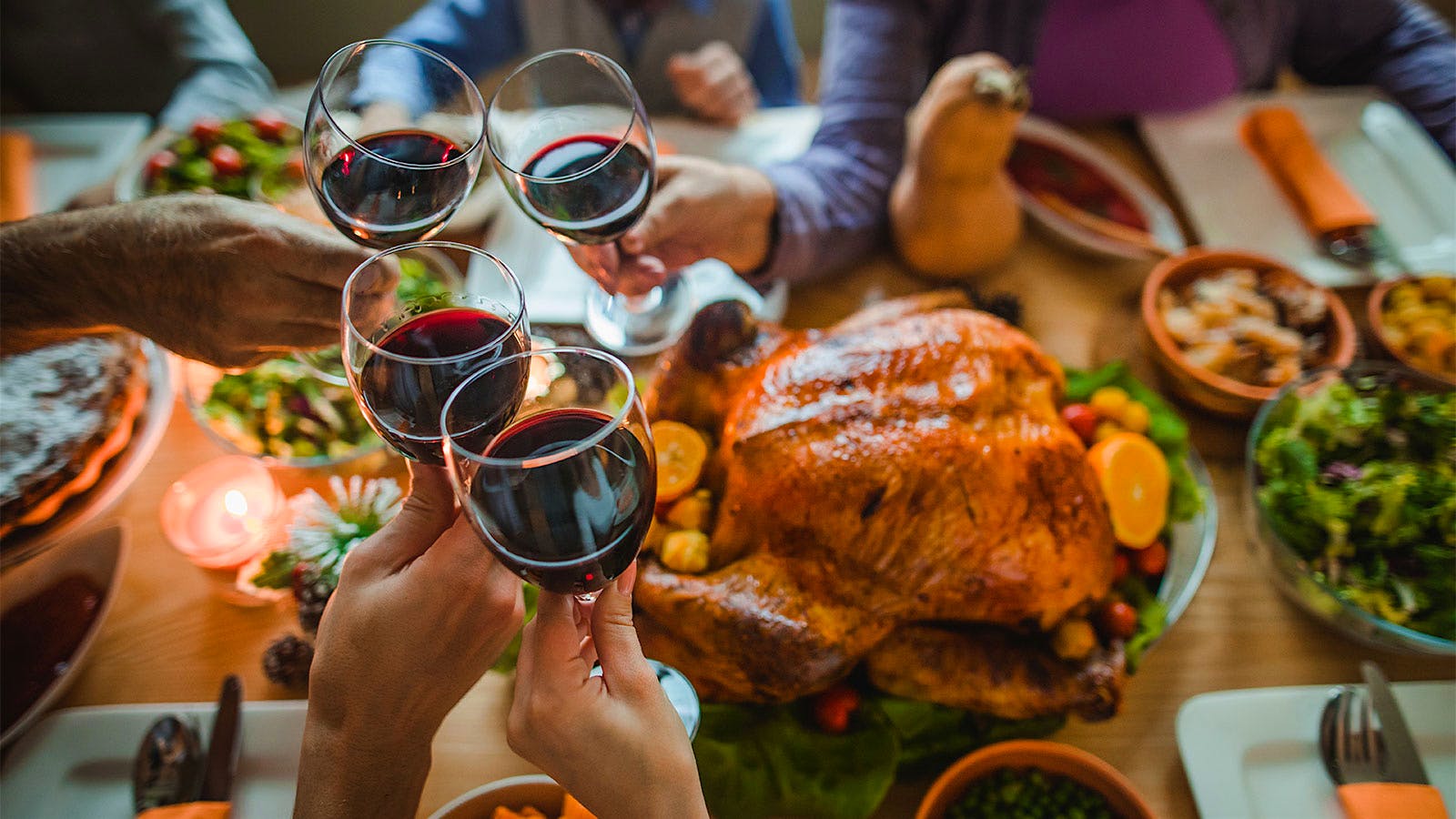Turkey and other Thanksgiving dishes on a table as people clink glasses of red wine